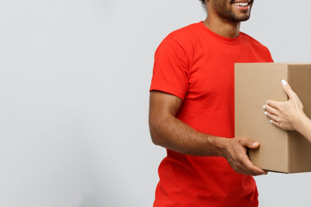 delivery concept handsome african american delivery man giving package to homeowner. isolated on grey studio background. copy space.